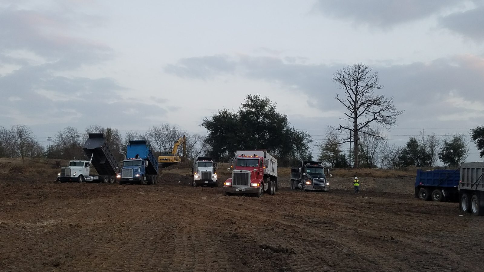 GMS multi-truck mobilization with six dump trucks and Komatsu excavator coordinating fill delivery at active Greater Houston jobsite